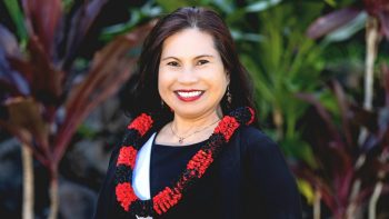 Luzviminda Miguel formal portrait, wearing red and black lei, outdoor setting.